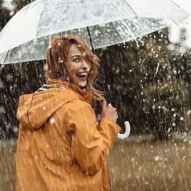 Junge Frau in einer orangenen Jacke und einem Schirm ist ausgelassen fröhlich, obwohl es regnet