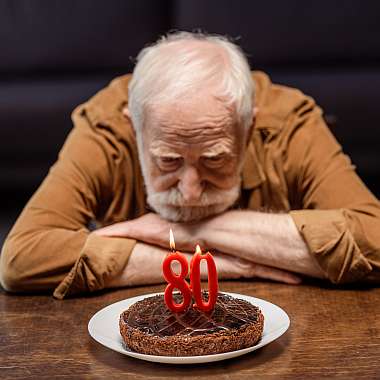 Alter Mann schaut frustriert auf seinen Geburtstagskuchen zum Jubiläum weil er keine Eventversicherung hatte.