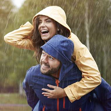 Junger Mann nimmt seine Frau im Regen Huckepack und beide sind dabei ausgelassen fröhlich
