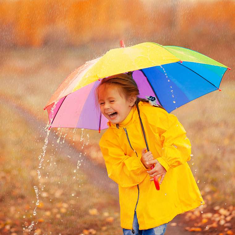 Junges Mädchen mit Schirm freut sich über den Regen im Urlaub und spielt damit